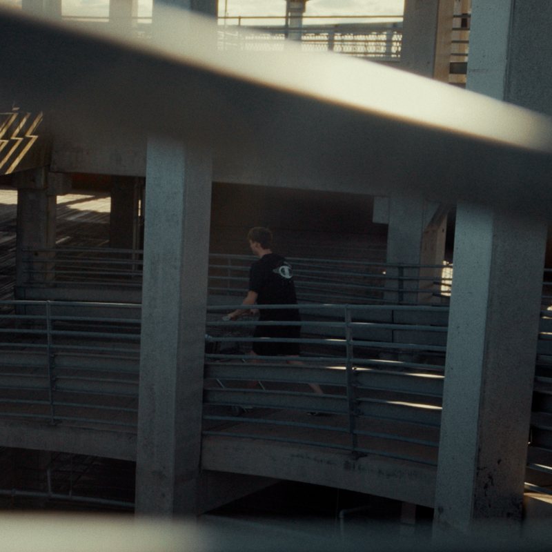 Mande walking through a parking garage in a black tee with a Champion back print